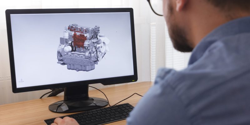 Engineer, Constructor, Designer in Glasses Working on a Personal Computer. He is Creating, Designing a New 3D Model of Car Engine, Motor in CAD Program. Freelance Work Engineer, Constructor, Designer in Glasses Working on a Personal Computer. He is Creating, Designinga New 3D Model of Car Engine, Motor in CAD Program. Freelance Work.